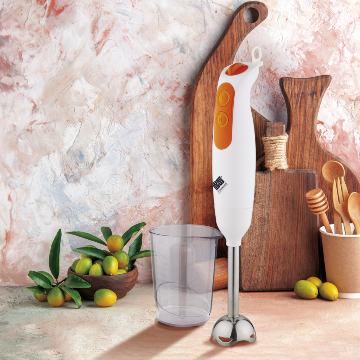 Batidora de mano blanca y naranja con accesorios y frutas.