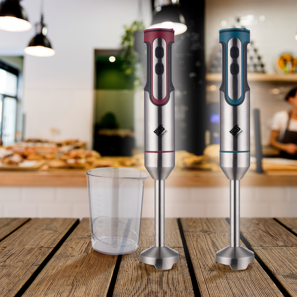 Dos batidoras de mano y un vaso medidor sobre una superficie de madera contra un interior de cafetería borroso.