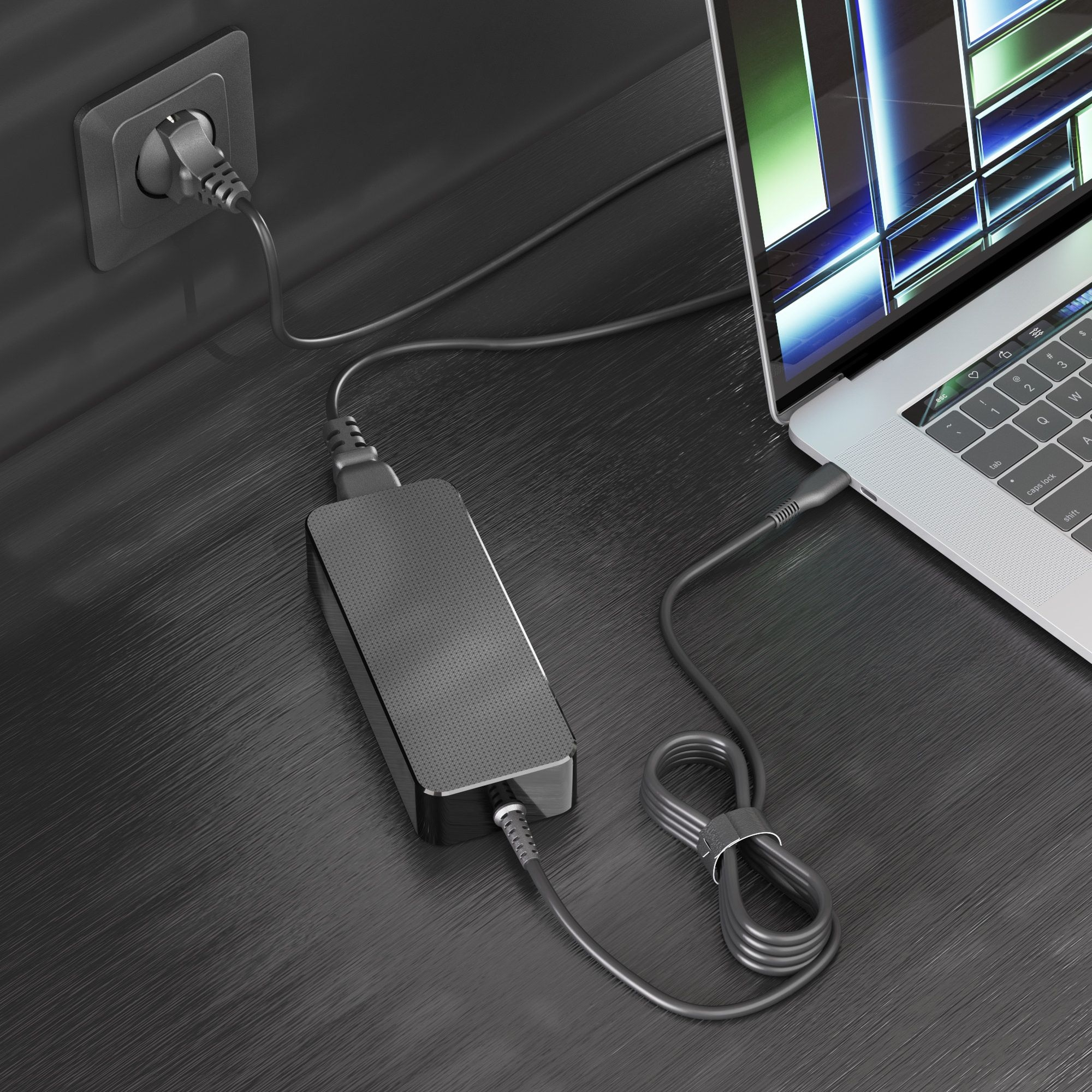 Laptop in carica con un adattatore collegato a una presa a muro. Il laptop è aperto su una superficie scura.