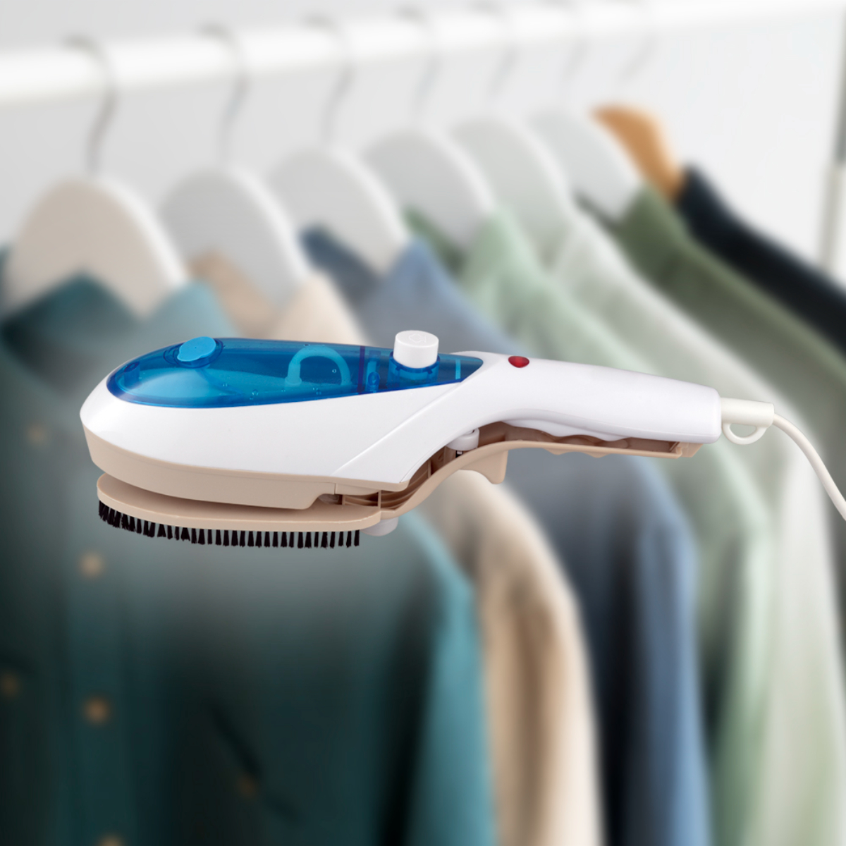 Vaporizador de ropa portátil blanco y azul con un cepillo marrón. Ropa colgando en el fondo borroso.