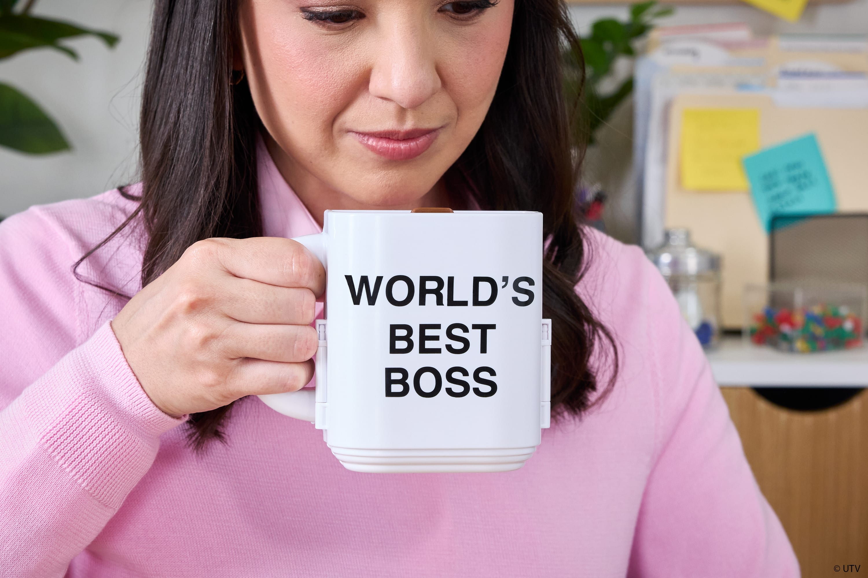 Kobieta trzymająca kubek z napisem "WORLD'S BEST BOSS", uśmiechając się.