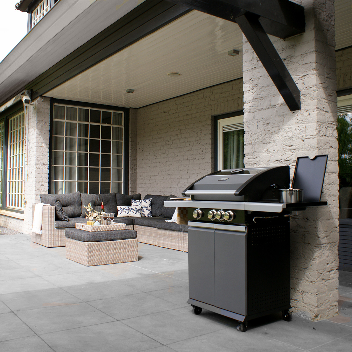 A grey brick patio with outdoor furniture and a grill under a covered patio area.
