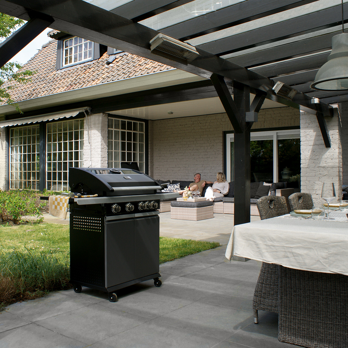 A black grill on a patio with people, furniture, and a house in the background.
