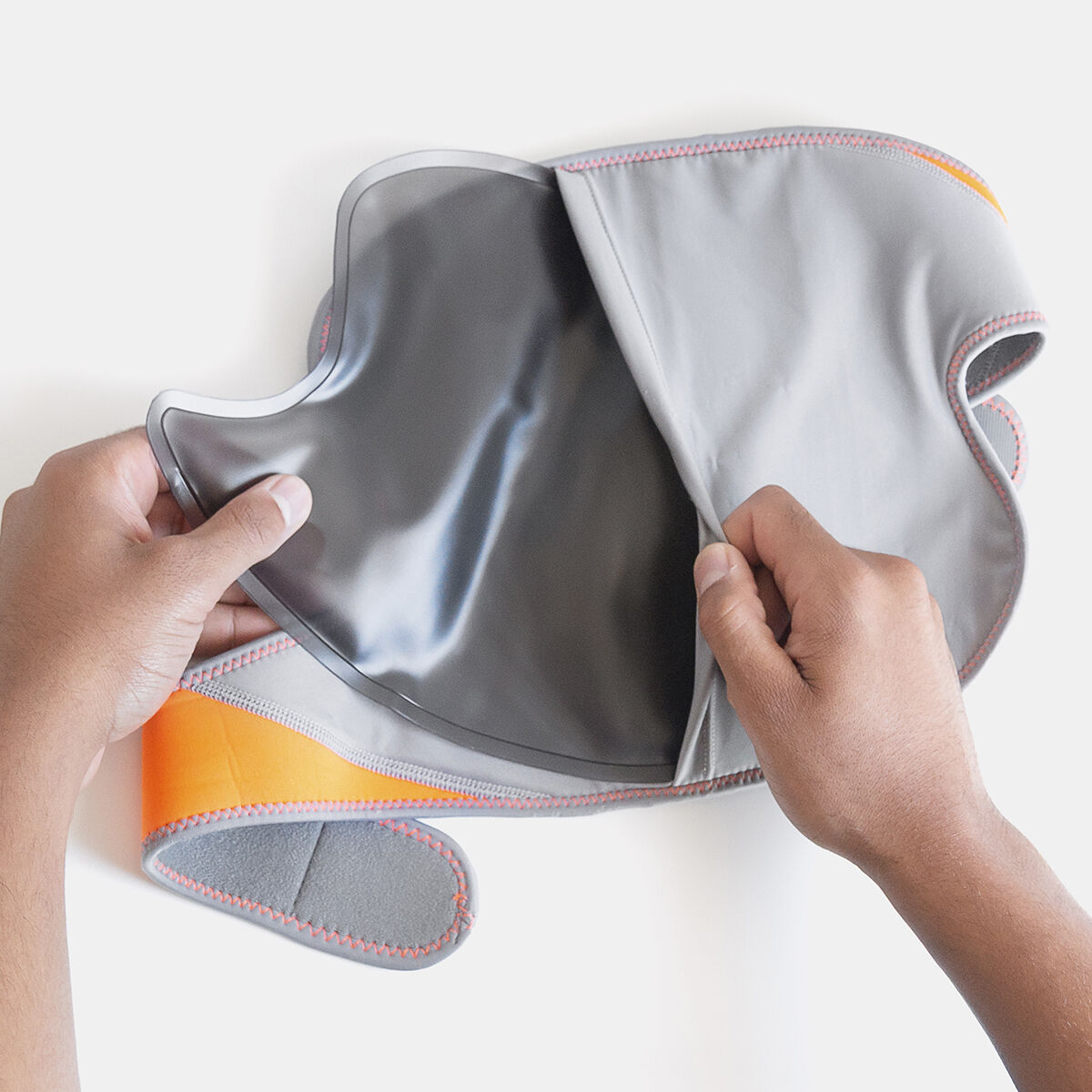 Manos sosteniendo una envoltura gris y naranja para la cara y el cuello, mostrando el interior.