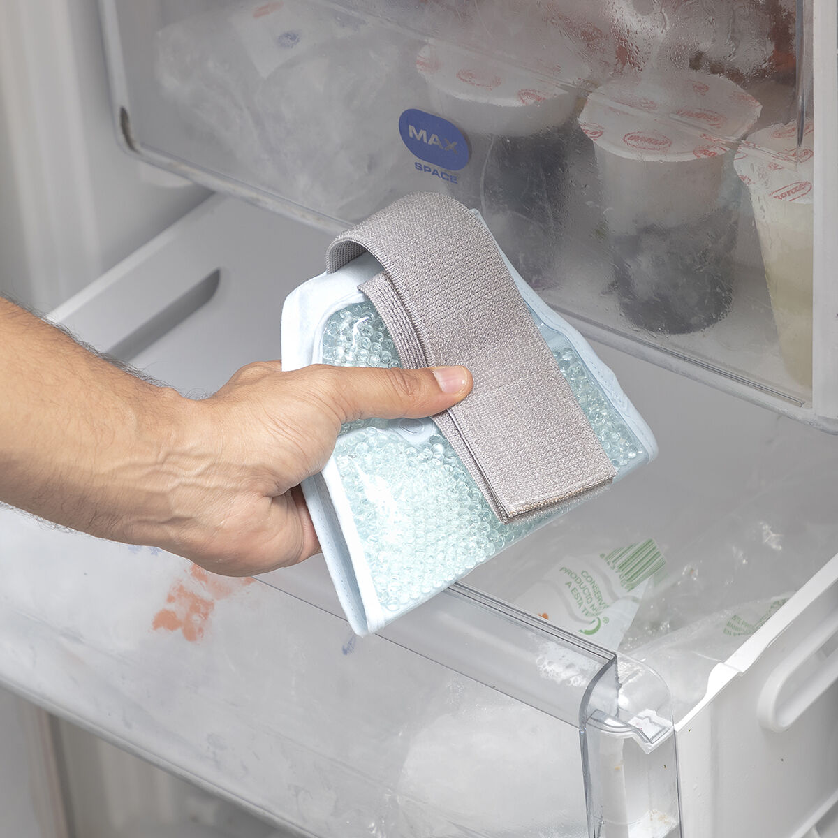 Una mano che mette un impacco di ghiaccio in un cassetto del frigorifero.