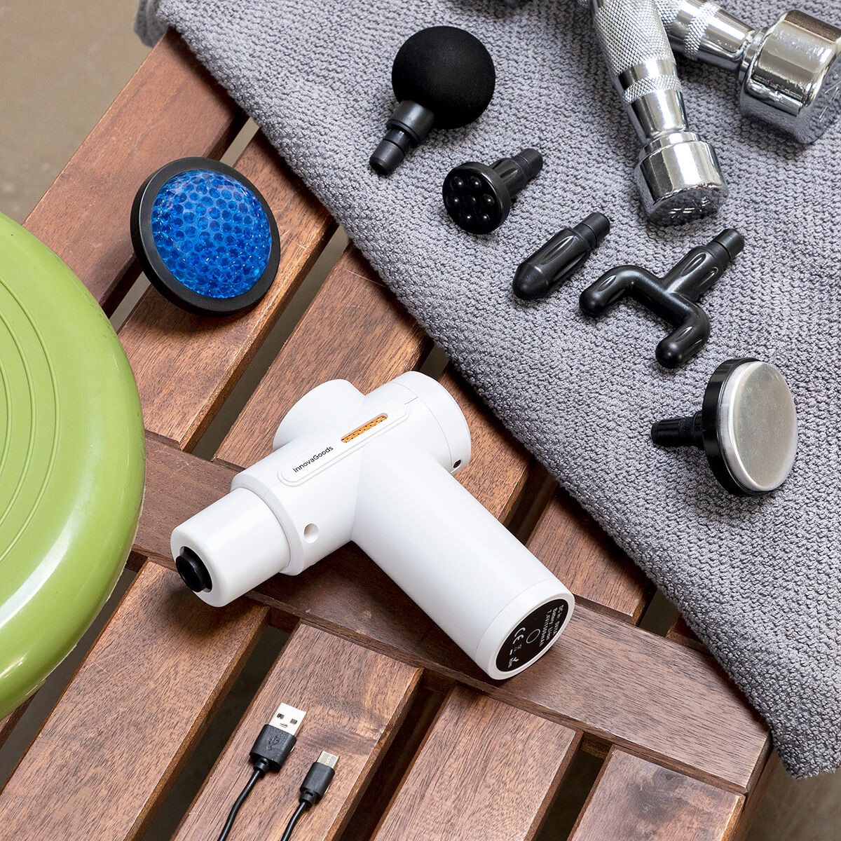 Una pistola de masaje blanca con varios accesorios, colocada sobre una superficie de madera con accesorios.