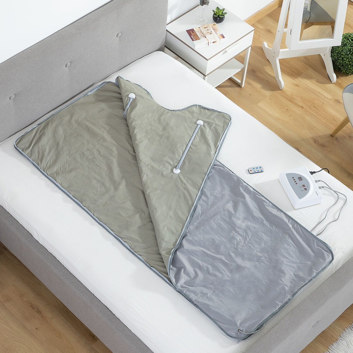 Un letto con una coperta grigia, un pannello di controllo e un telecomando. È presente anche un comodino con decorazioni.