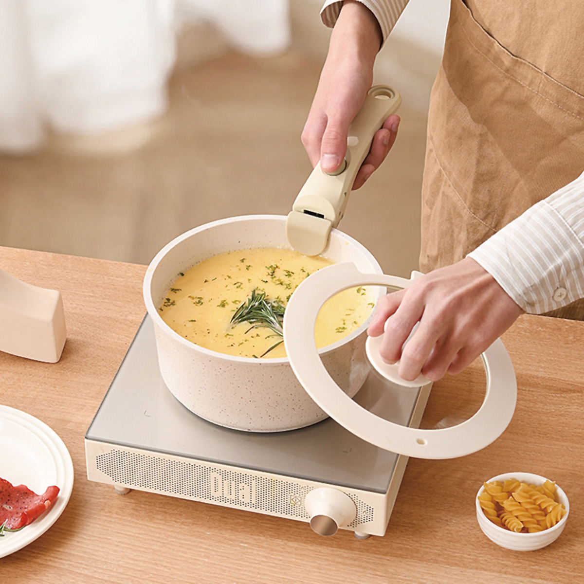 Persona cocinando sopa en una olla blanca sobre una estufa beige. Una persona sostiene una tapa y un mango.