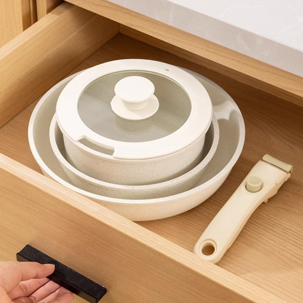 Ollas blancas y beige en un cajón. Un asa y una tapa están junto a las ollas. Cajón de madera.