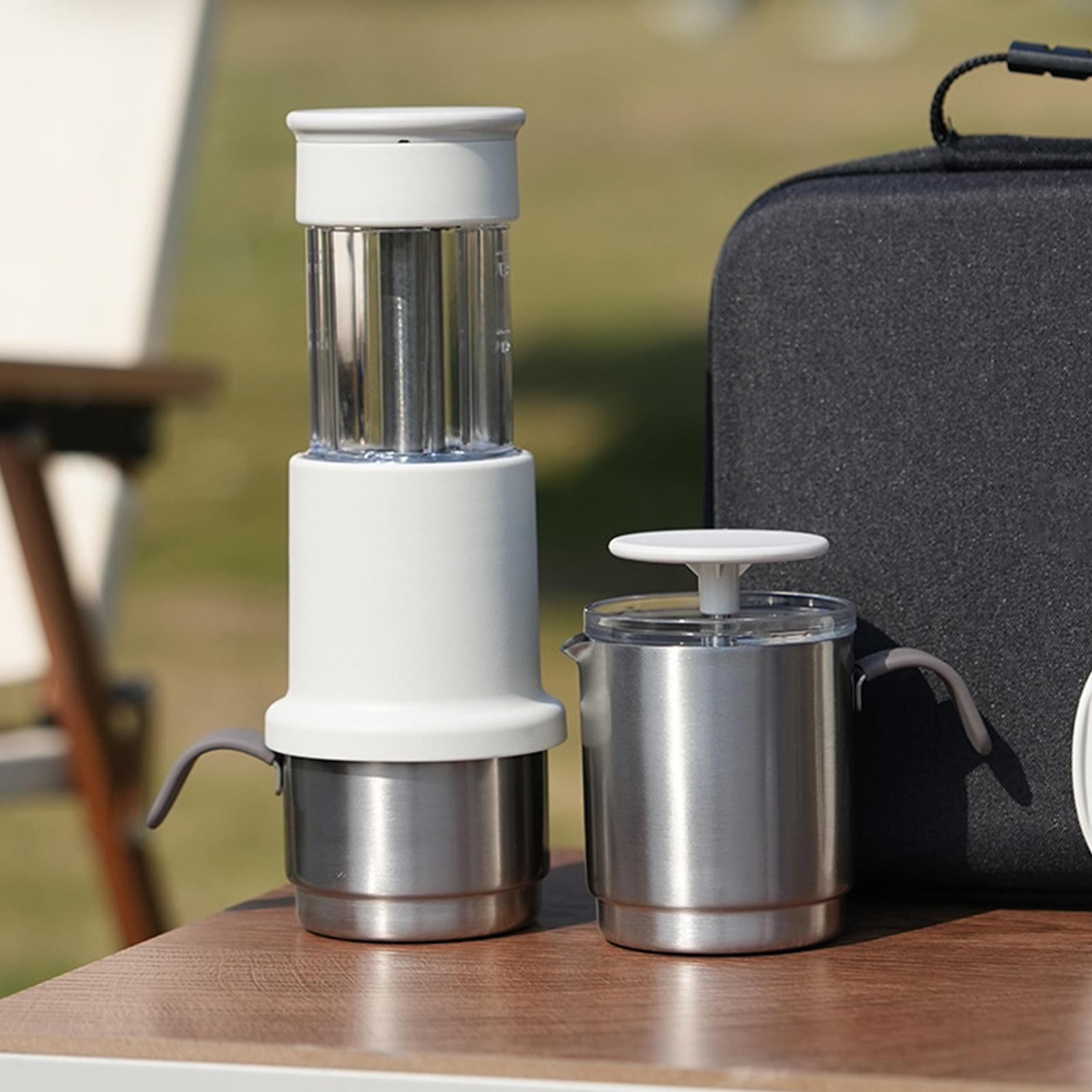 Eine Kaffeemaschine und eine Edelstahlkanne auf einem Holztisch, im Hintergrund eine schwarze Tasche.