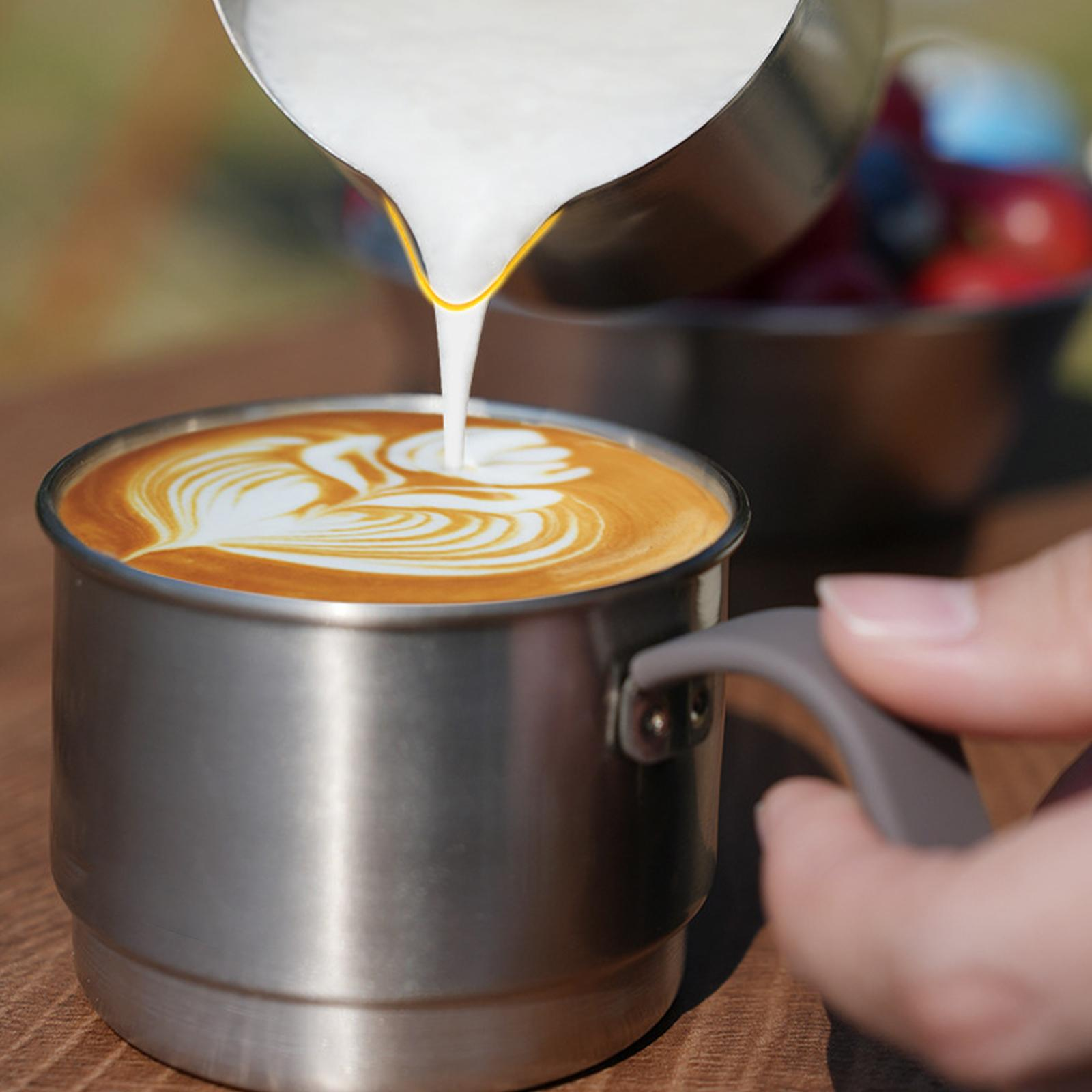 Milch wird in einen Kaffee gegossen. Kaffee-Kunst ist in der Edelstahl-Tasse sichtbar.