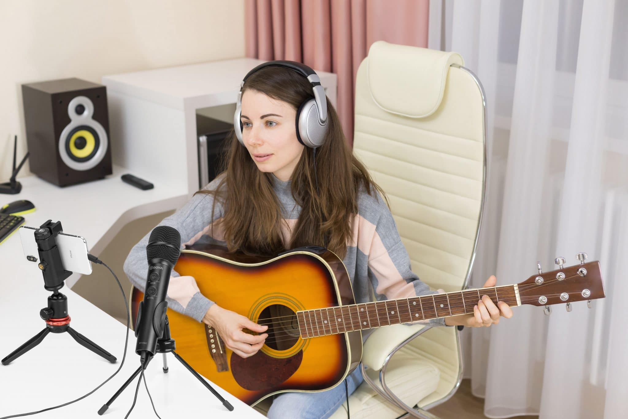 Frau mit Kopfhörern, Gitarre spielend, Mikrofon für Aufnahmen eingerichtet.