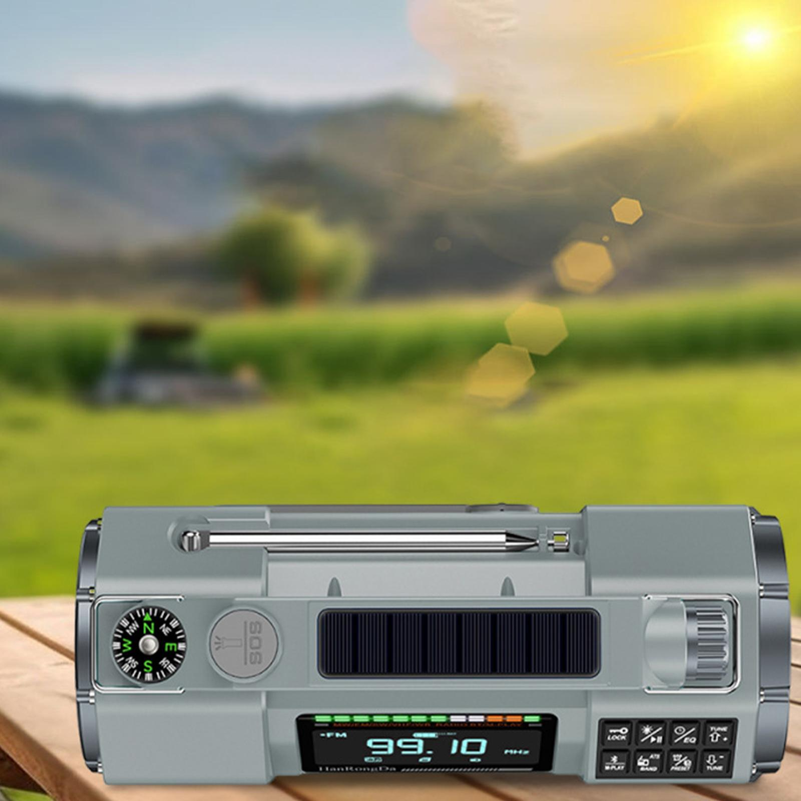 Graues Radio mit Kompass auf einem Holztisch. Hintergrund: grünes Feld und sonniger Himmel.