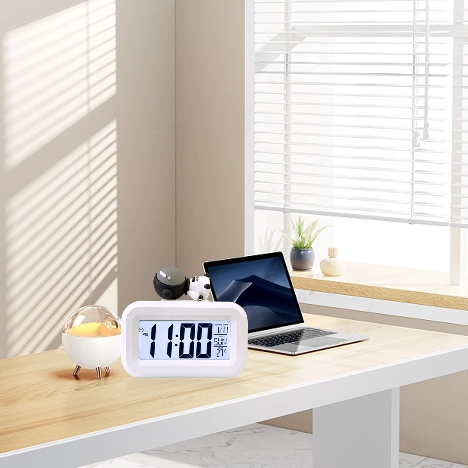 Eine Digitaluhr zeigt 11:00 Uhr an. Sie steht auf einem Schreibtisch, neben einem Laptop, einer Dekokugel und einem Fenster.
