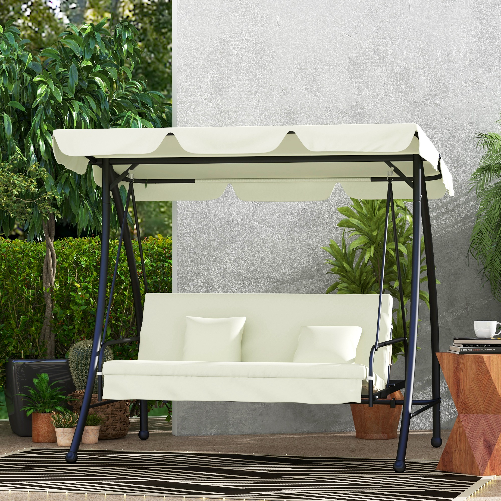 Ein cremefarbenes Schaukelgestell mit schwarzem Rahmen, Baldachin und Kissen, auf einer Terrasse mit Pflanzen.