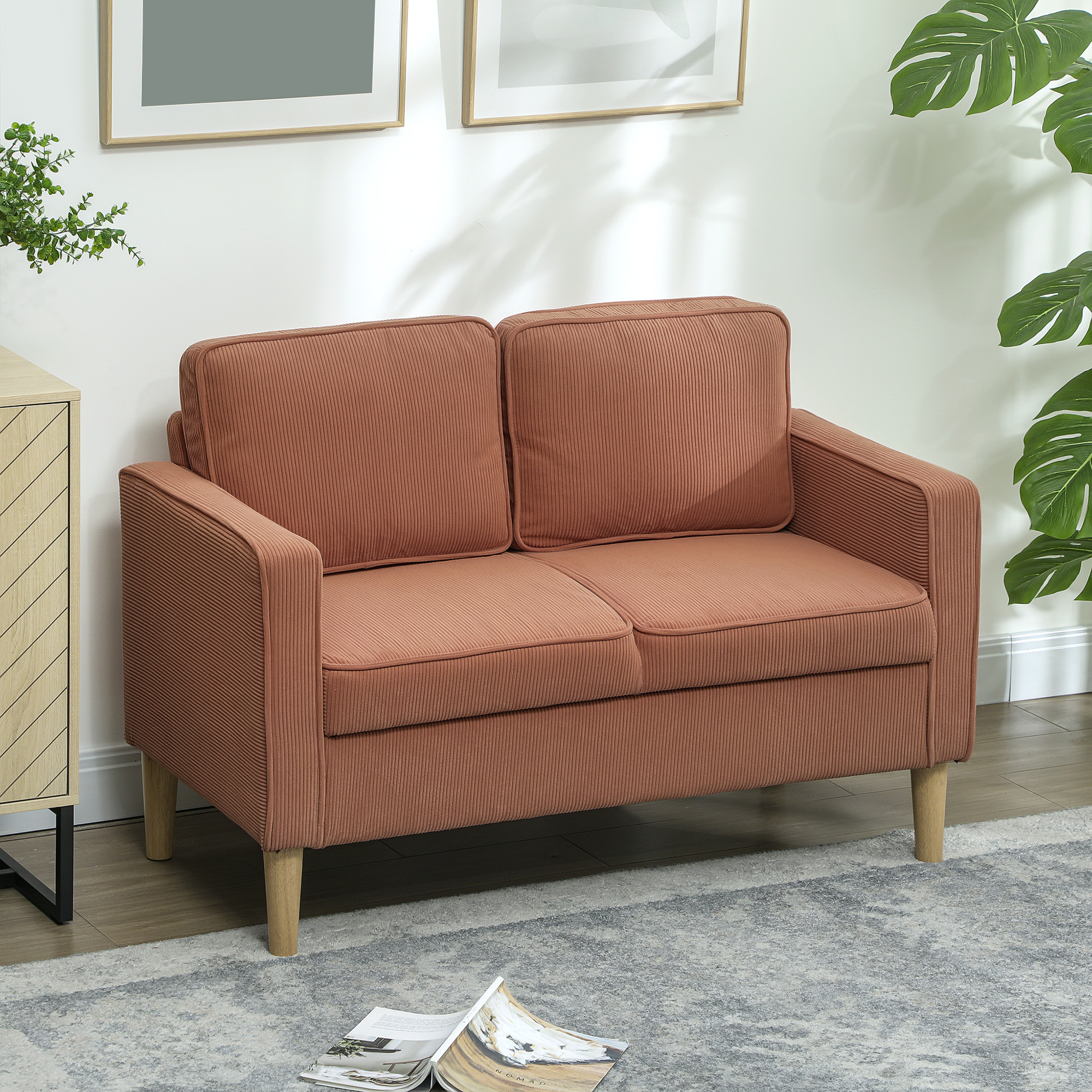 Braunes Cordsofa mit zwei Kissen, Holzbeinen und einem grauen Teppich. Bilder an der Wand.
