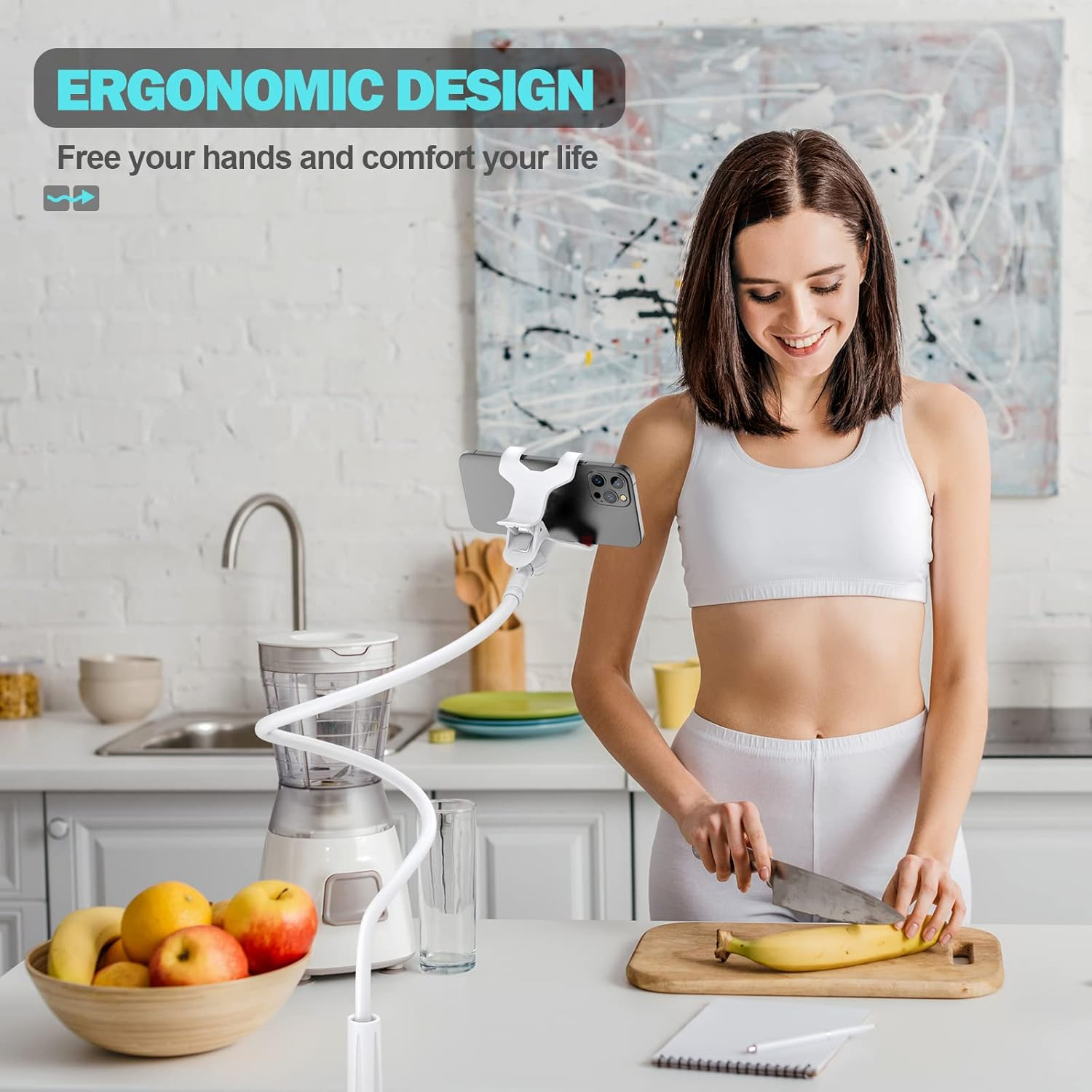 Frau schneidet eine Banane mit einem Messer, verwendet einen flexiblen Telefonhalter. Früchte und eine Schüssel sind sichtbar.