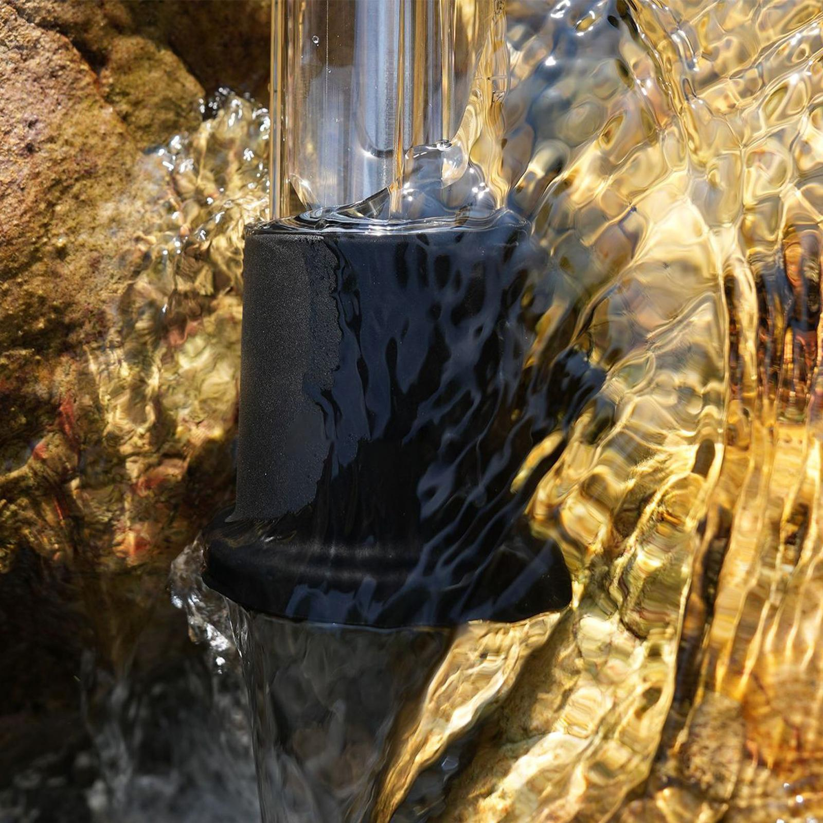 Nahaufnahme von Wasser, das um ein schwarzes zylindrisches Objekt mit einem klaren Rohr und Felsen fließt.