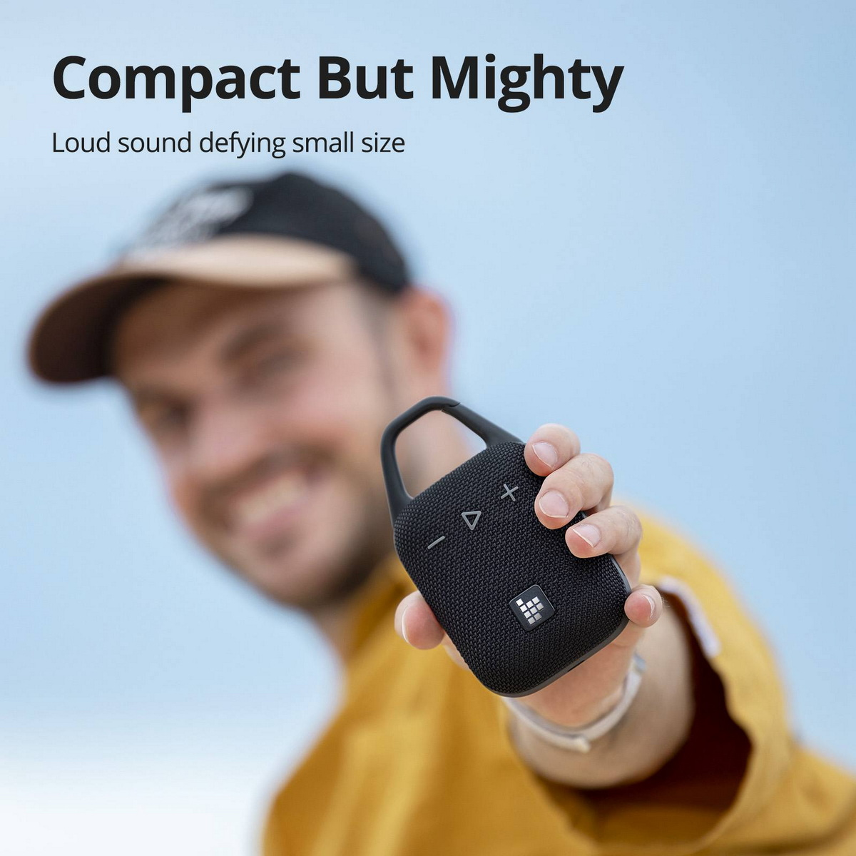 Person hält einen schwarzen Lautsprecher. Text lautet: Compact But Mighty. Lauter Sound trotz kleiner Größe.