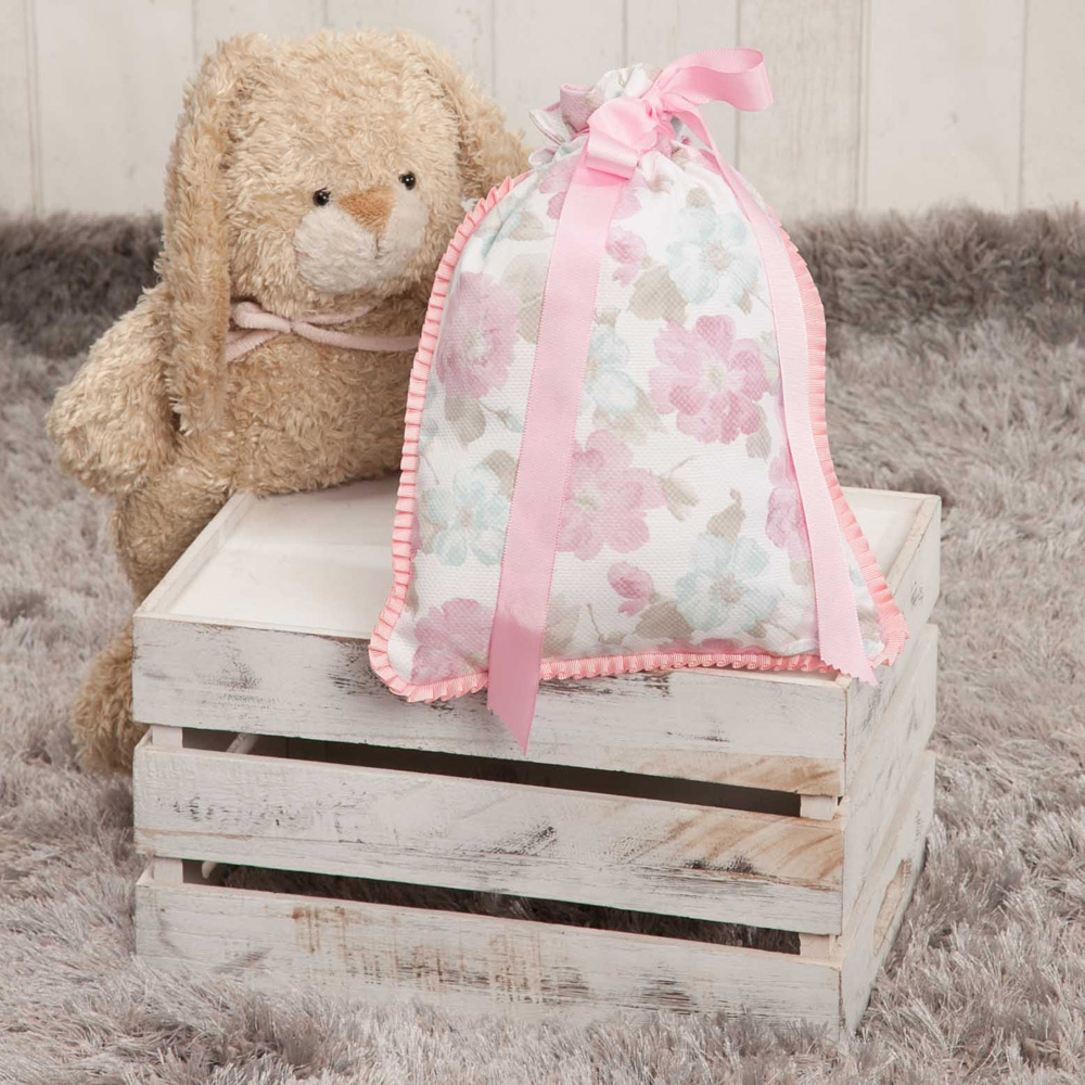 Una bolsa de regalo en una caja blanca con un osito de peluche. Flores rosas y cintas en la bolsa.