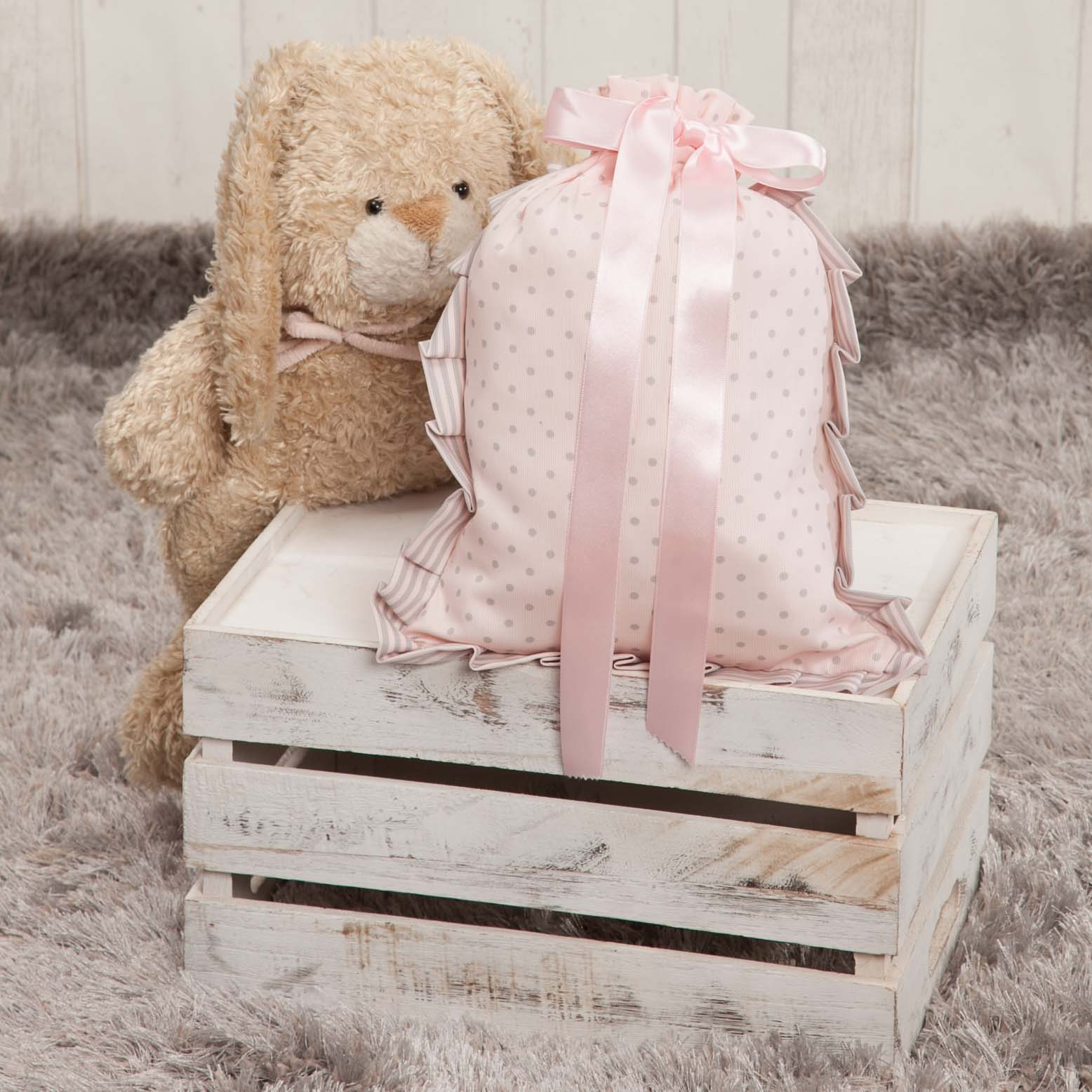 Bolsa rosa con lunares en una caja blanca con un oso de peluche. Fondo de alfombra gris.