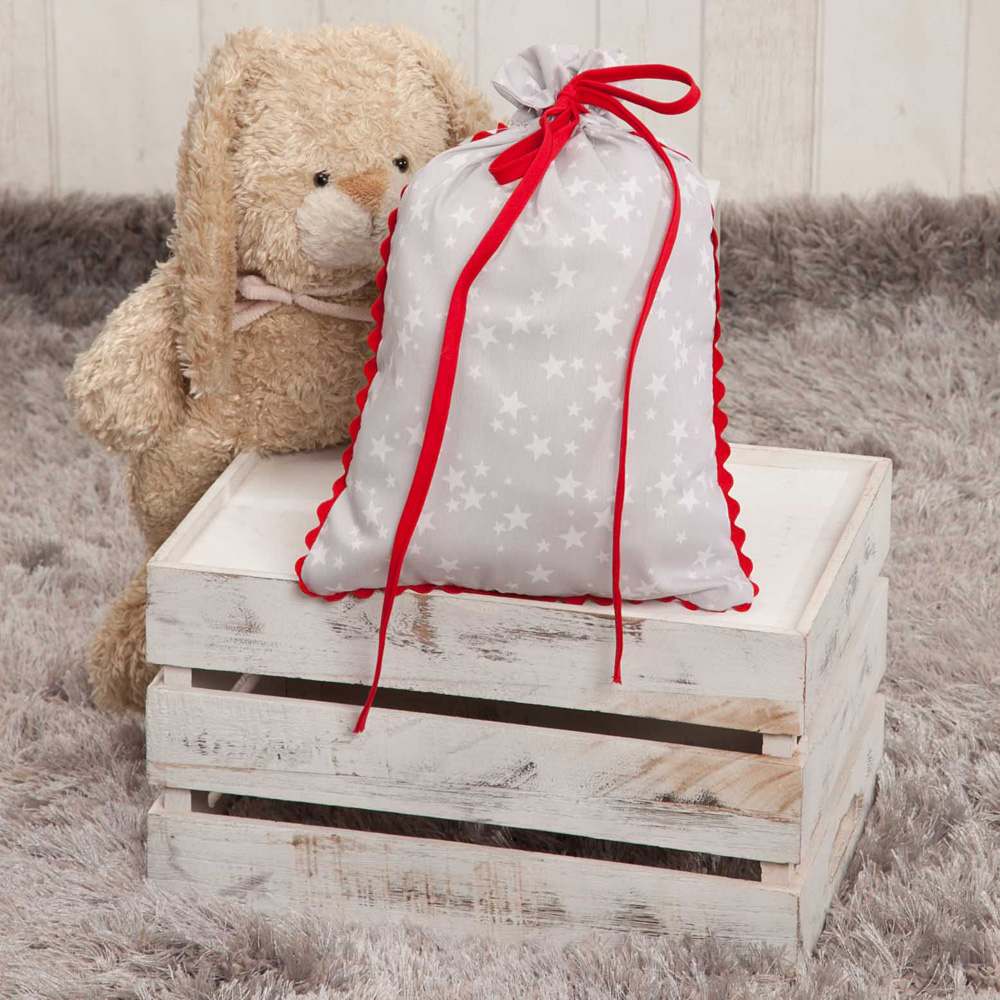 Bolsa gris con estrellas blancas sobre una caja blanca con un oso de peluche. Alfombra gris.