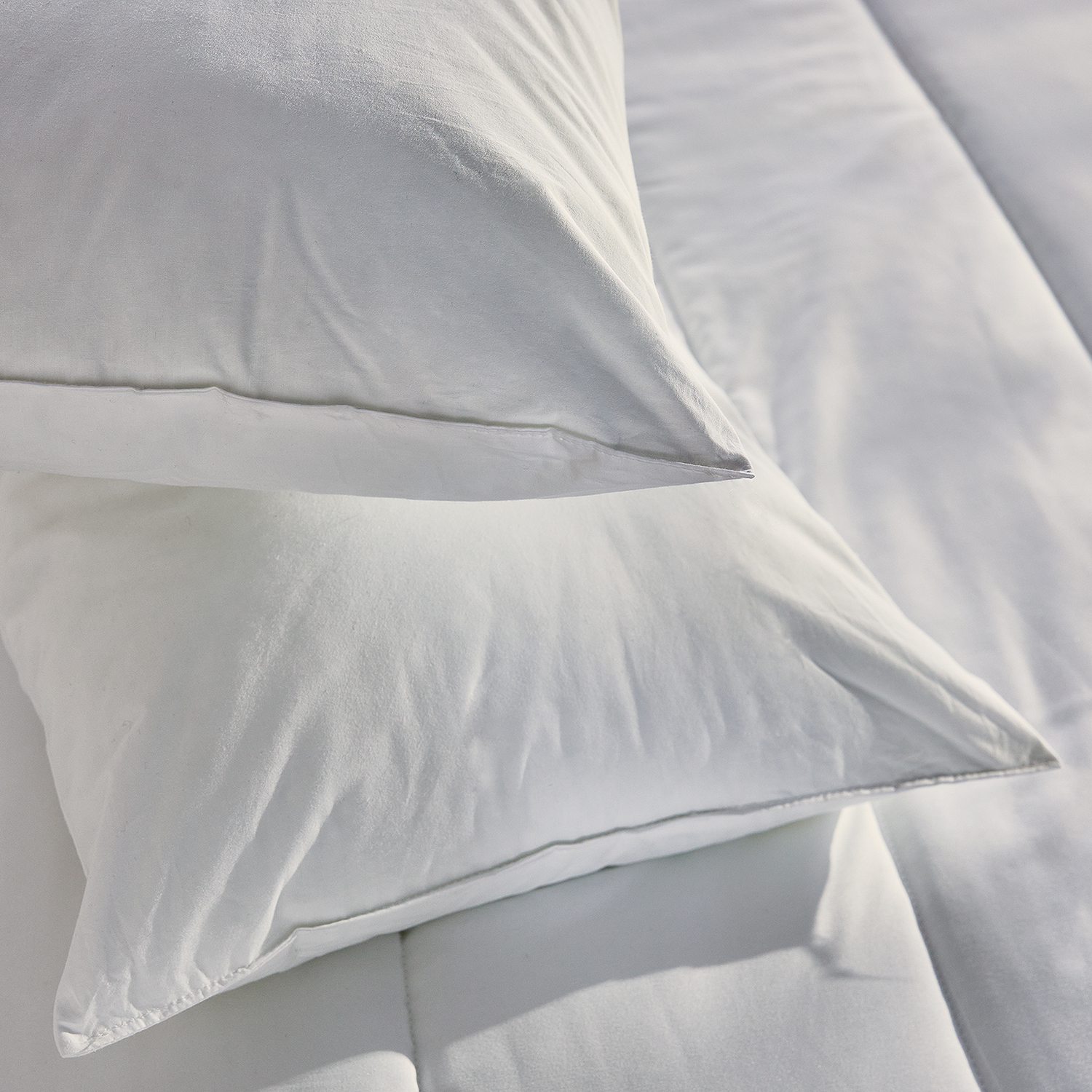 Primer plano de dos almohadas blancas. Las almohadas están sobre ropa de cama blanca. El fondo es blanco.