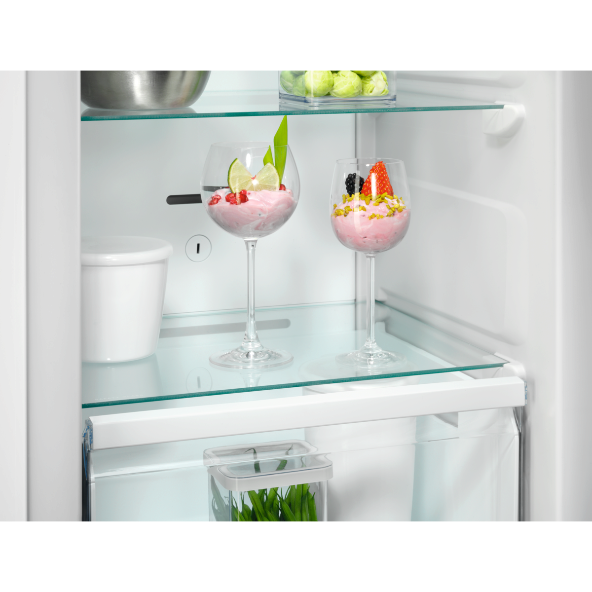 Estante de refrigerador con dos copas de postre, una con crema rosa y bayas.