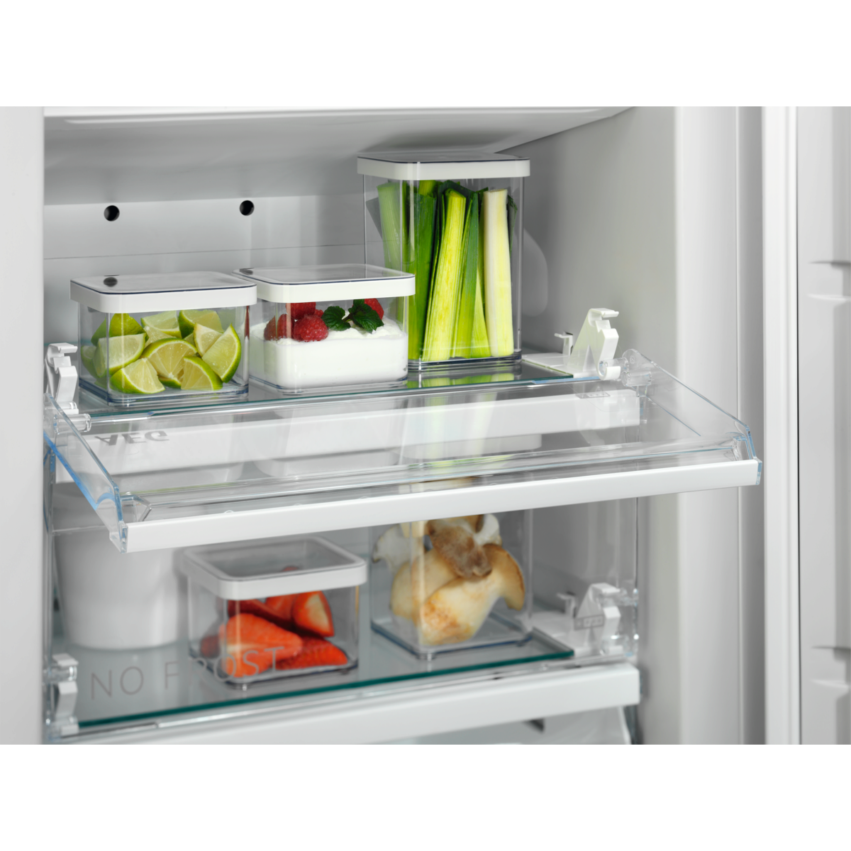 Interior de refrigerador con productos en recipientes transparentes: limas, bayas, puerros y fresas.