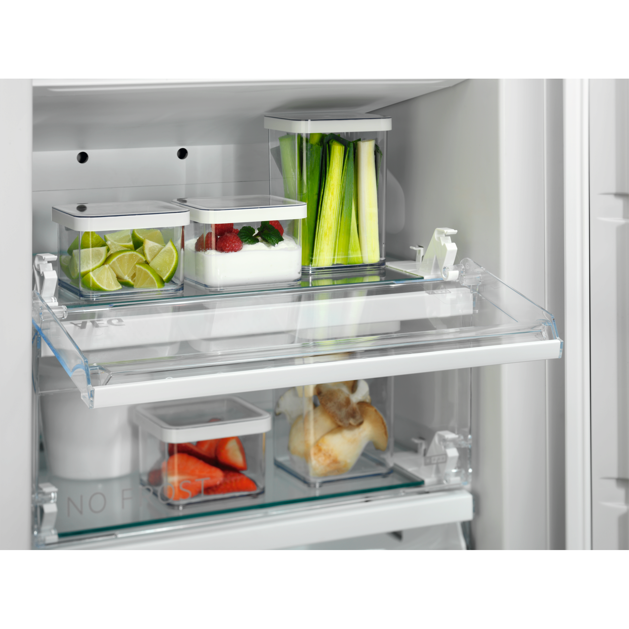 Interior de refrigerador con productos en recipientes transparentes: limas, bayas, puerros y fresas.
