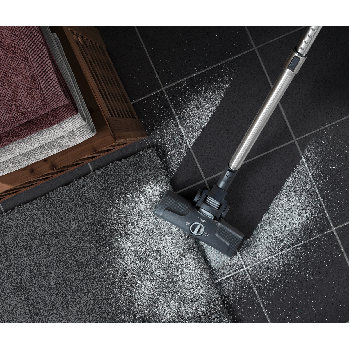 Odkurzacz czyszczący szary dywan na czarnej podłodze z płytek. Ręczniki i kosz w tle.