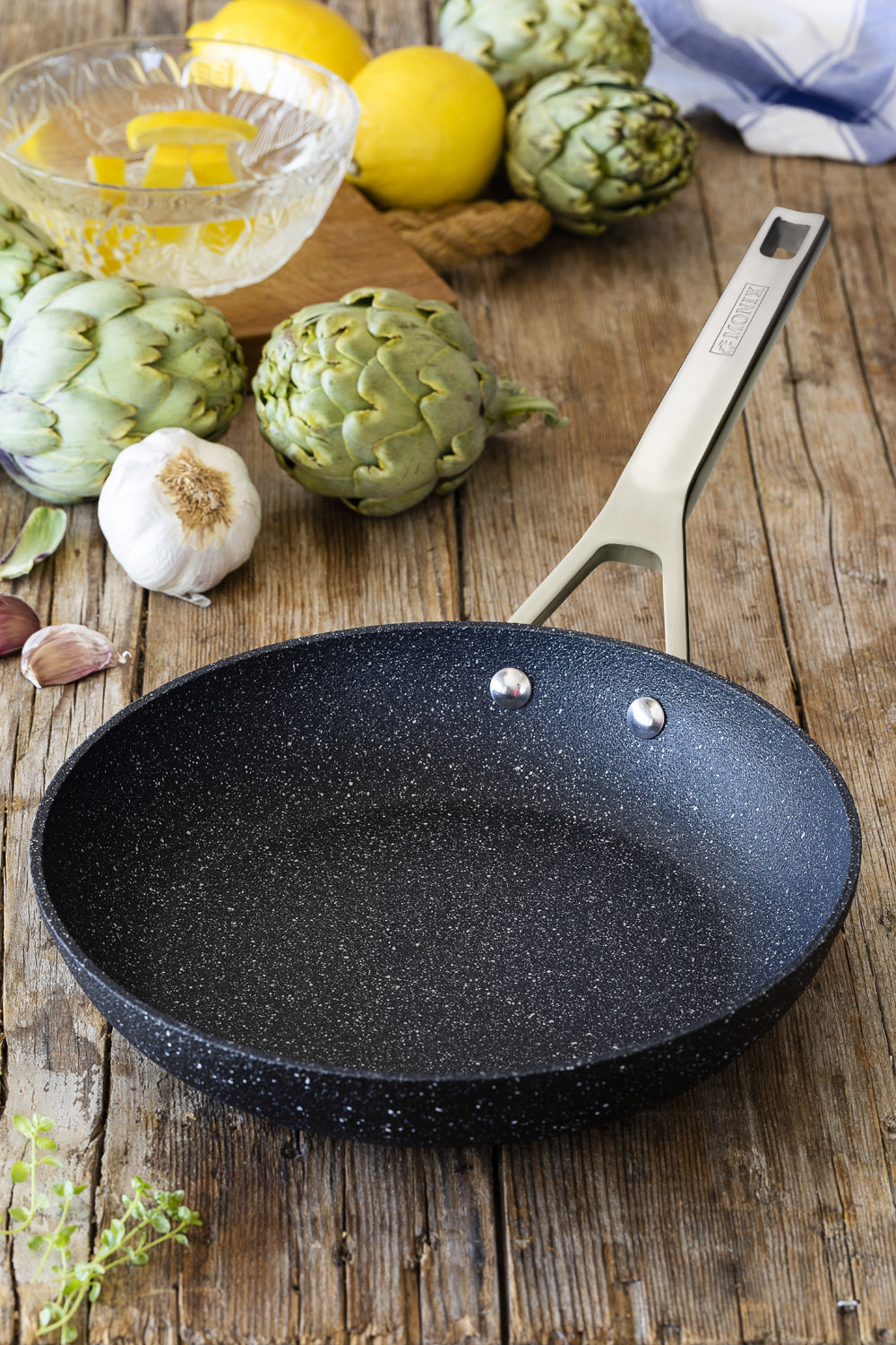 Patelnia na drewnianym stole z karczochami, cytrynami i czosnkiem. Uchwyt ze stali nierdzewnej. Rustykalne tło.