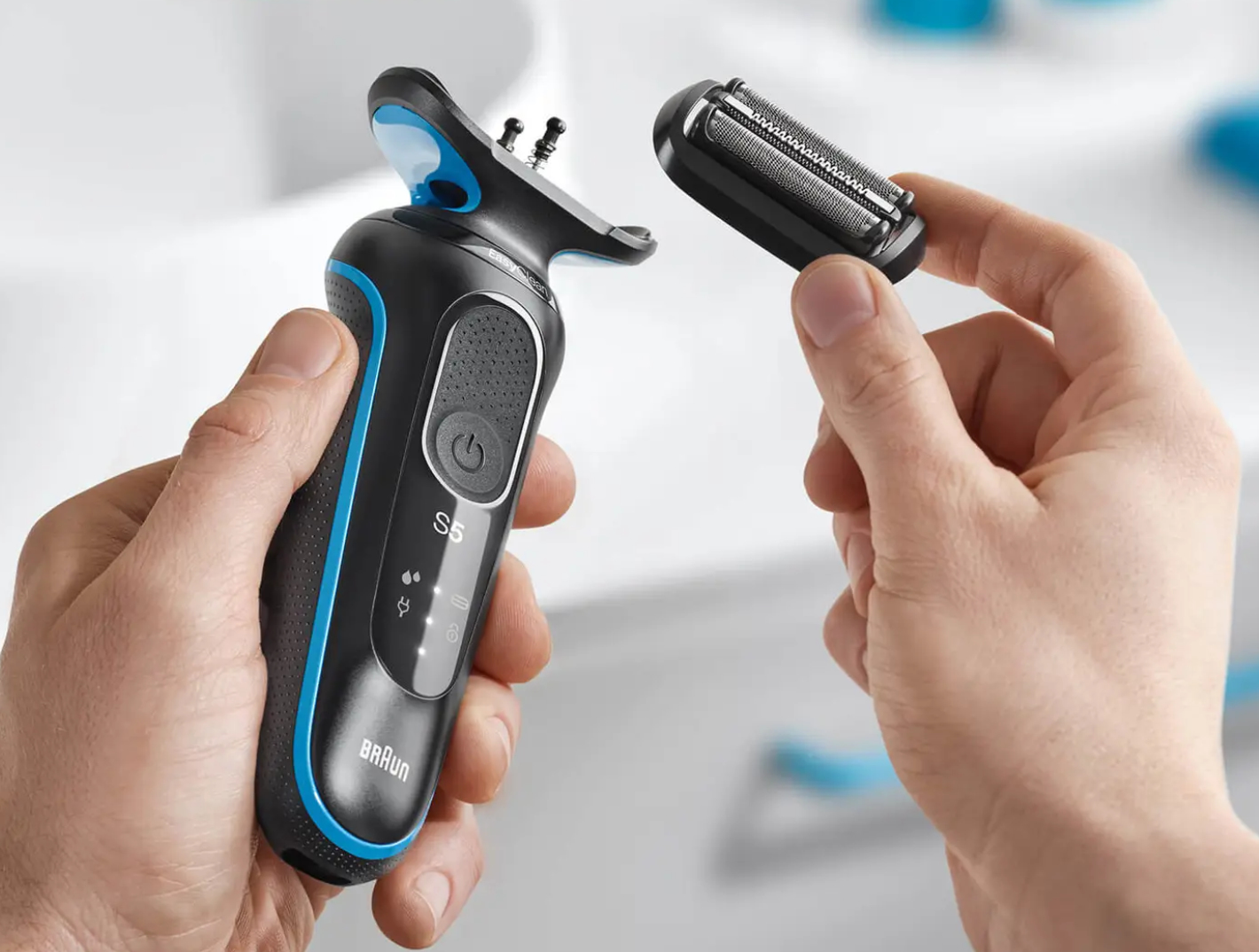 Osoba trzymająca czarno-niebieską golarkę elektryczną i jej wymienną głowicę.