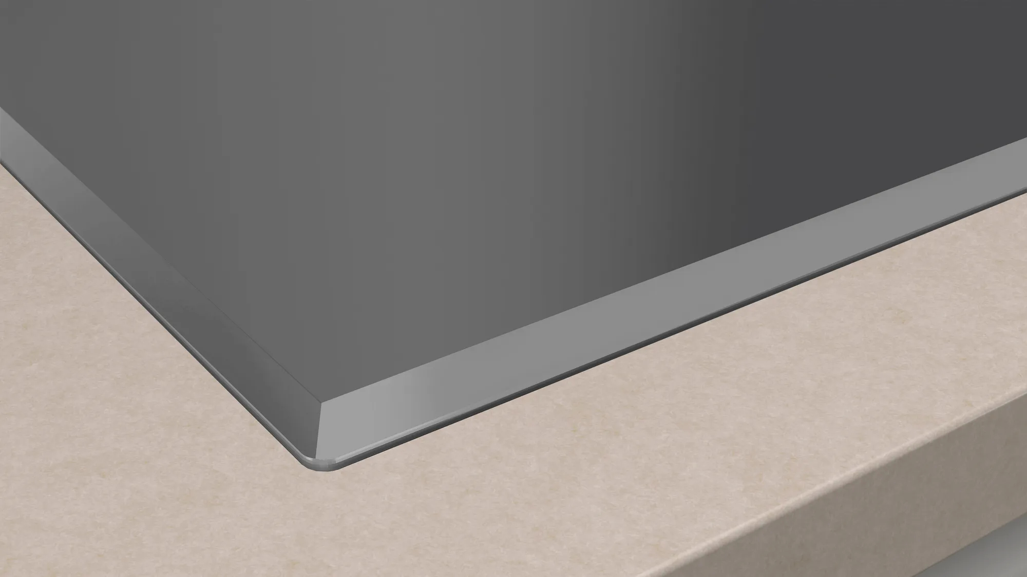 Zbliżenie ciemnoszarej płyty grzejnej na beżowym blacie. Krawędź płyty jest metaliczna.