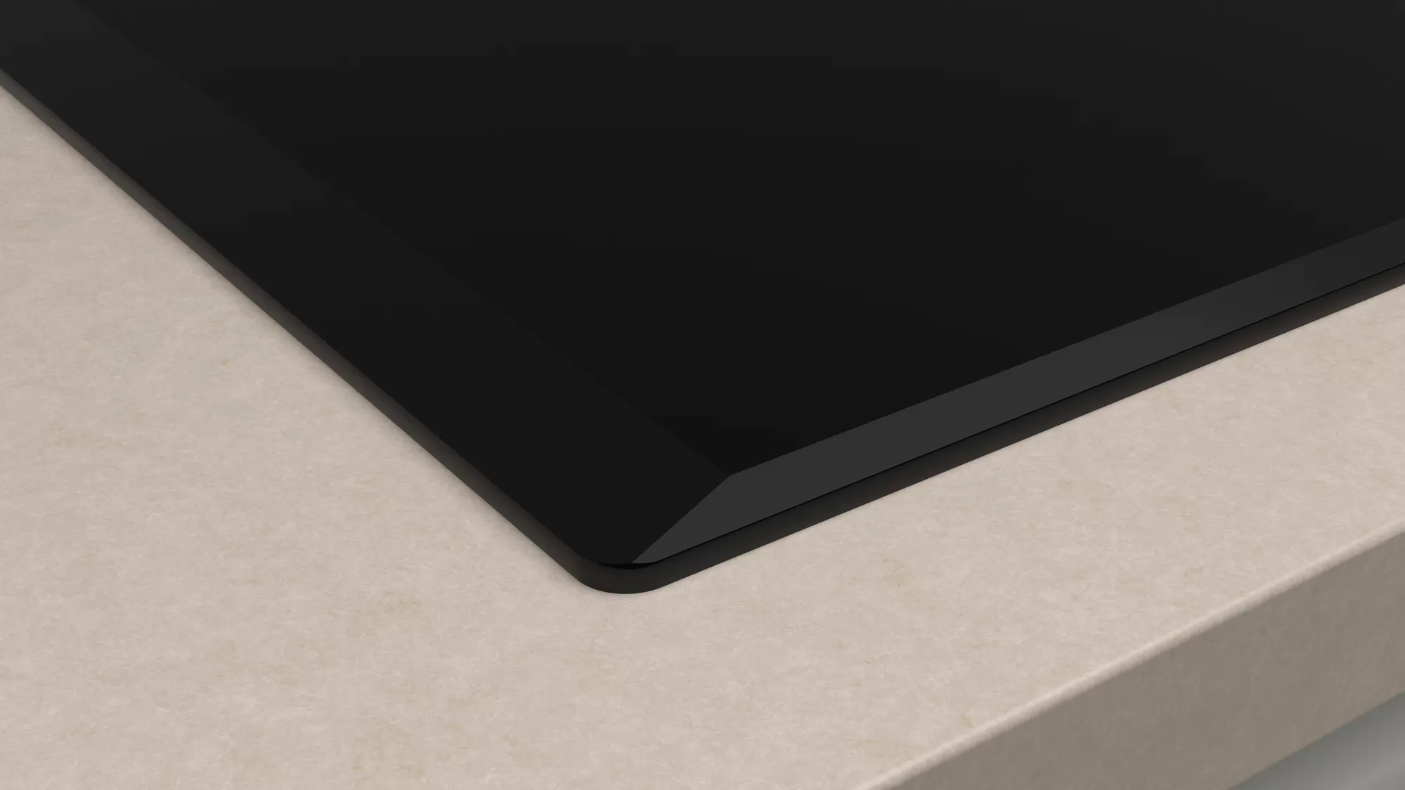 Róg czarnej płyty grzewczej na beżowej powierzchni. Ostra krawędź. Brak innych elementów.