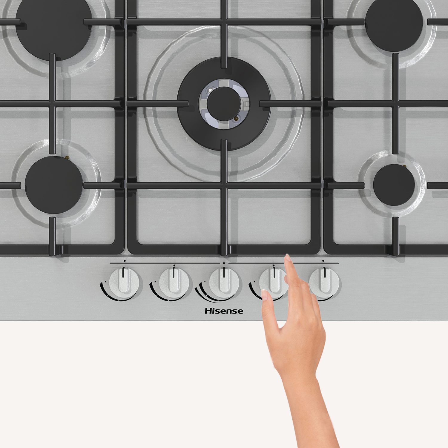 Srebrna płyta grzejna z pięcioma palnikami, dłoń sięga do pokręteł.