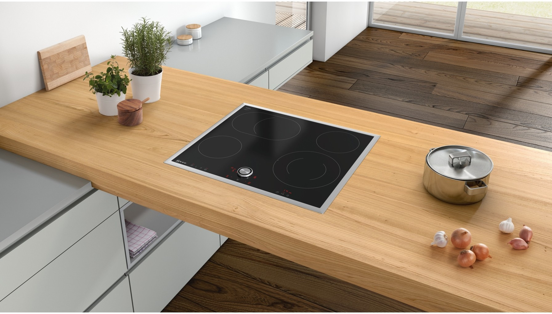Czarna płyta indukcyjna na drewnianym blacie. Widoczny garnek, zioła i cebula.