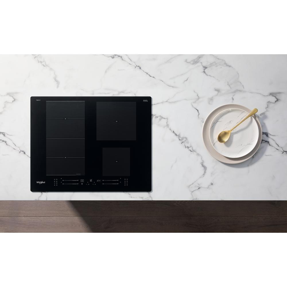 Placa de inducción negra Whirlpool en encimera de mármol, con plato y cuchara.