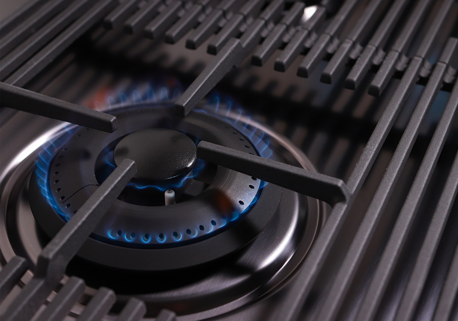 Primo piano di un bruciatore a gas con fiamme blu e griglie metalliche.