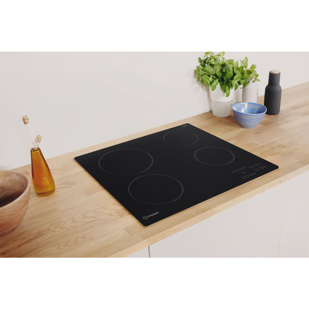 Placa de inducción negra con cuatro fuegos, encimera de madera y otros elementos de cocina.