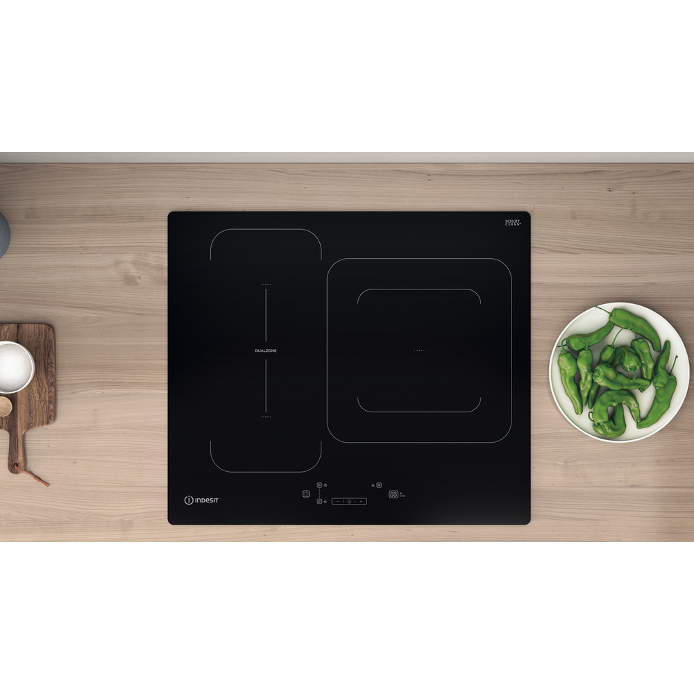 Vista superior de placa de inducción negra con dos quemadores y plato de pimientos.