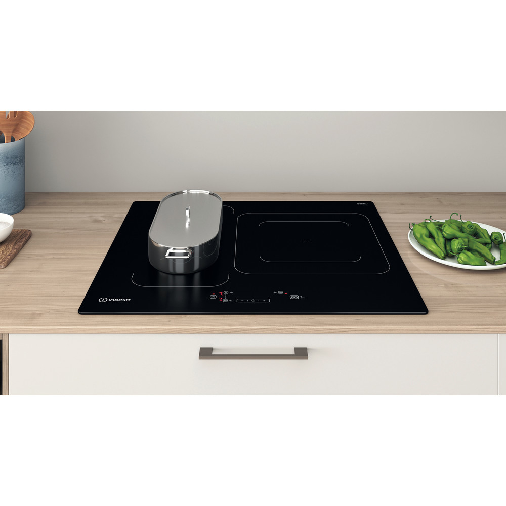 Placa de inducción negra con olla a la izquierda, pimientos verdes a la derecha.