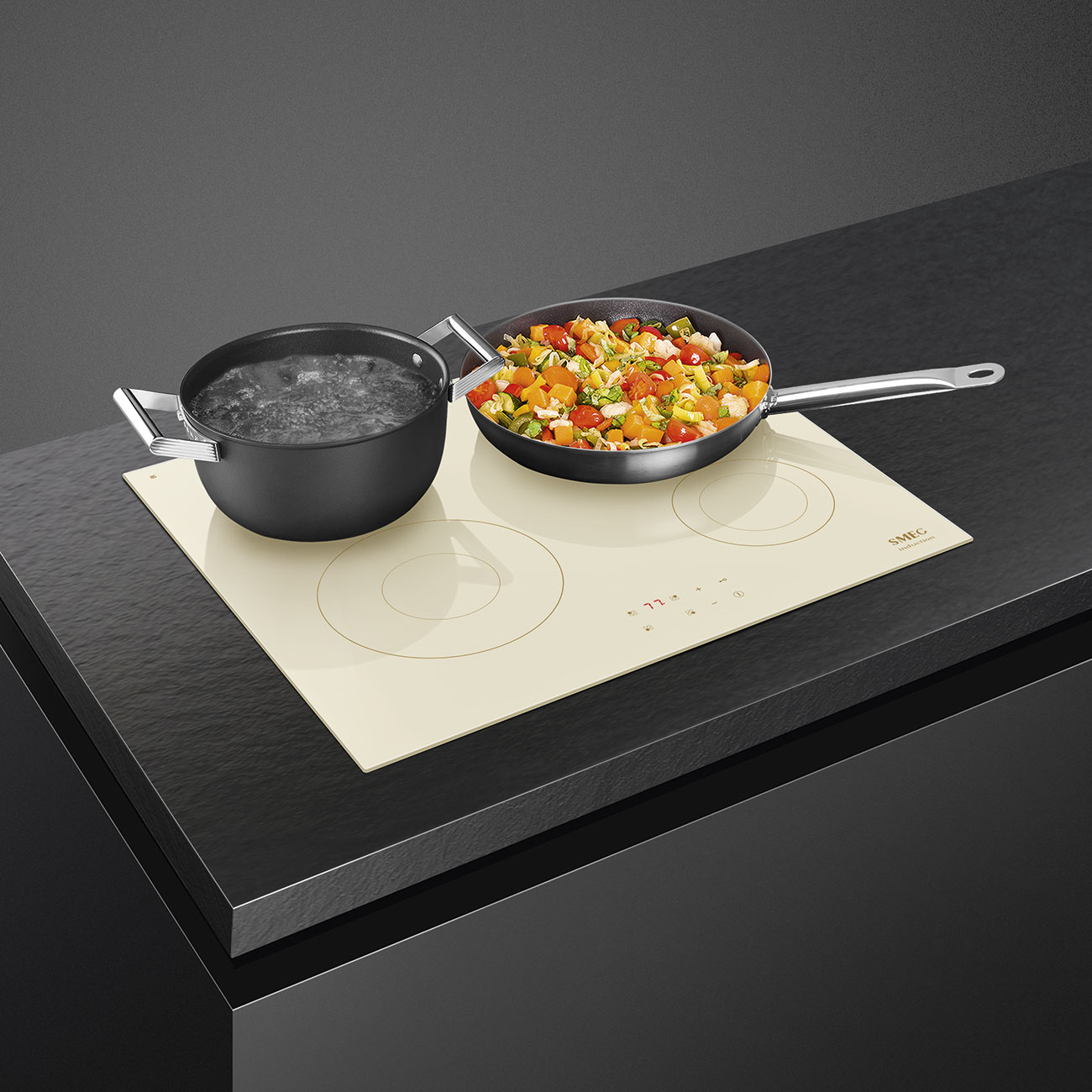 Piano cottura a induzione Smeg crema con due fuochi, pentola e verdure.