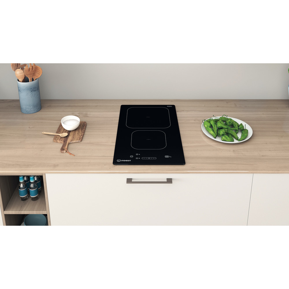 Piano cucina con piano cottura a induzione nero. Piatto di peperoni verdi a destra.
