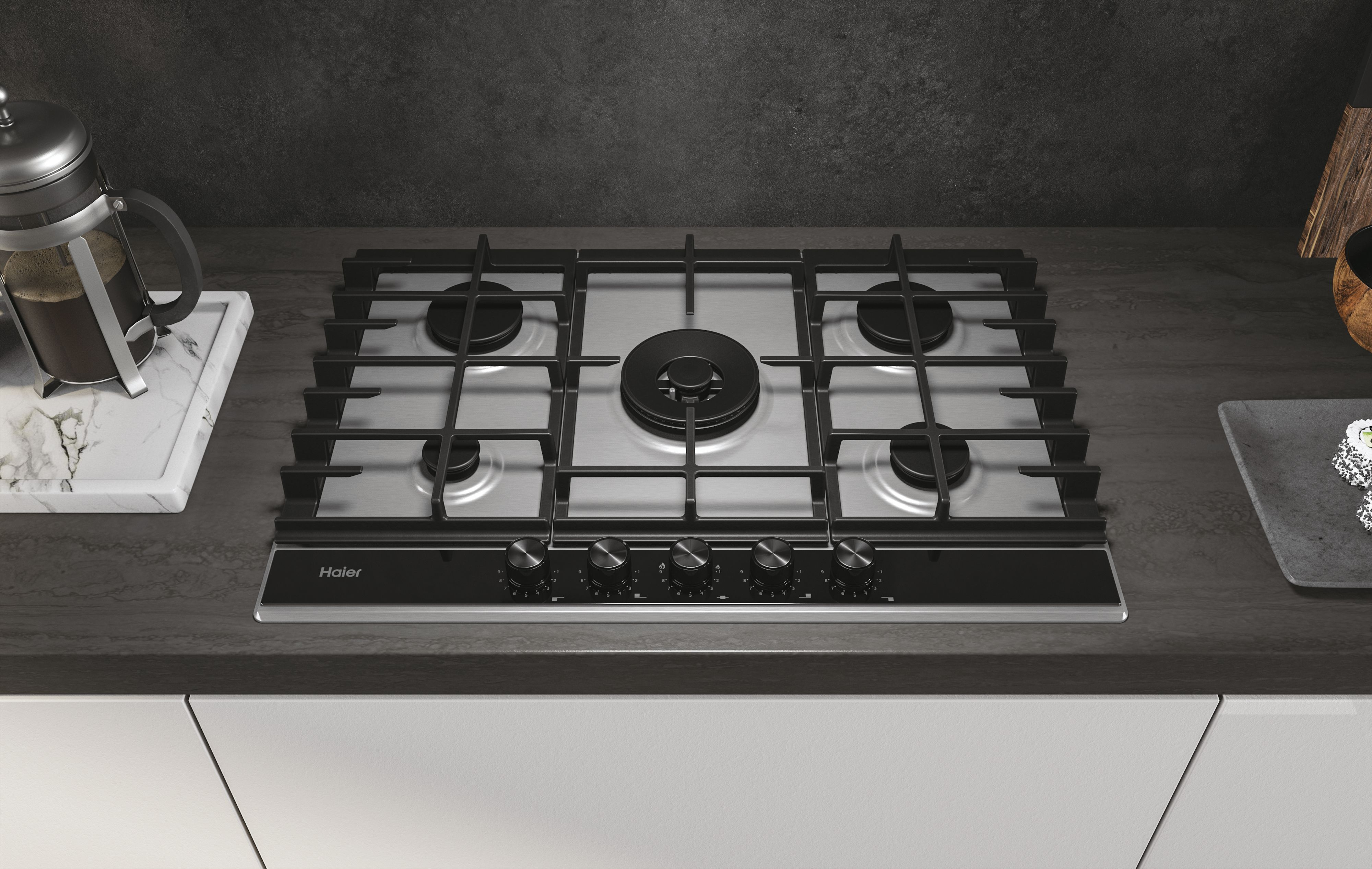 Ustawienie kuchenne ze stalową płytą gazową Haier i akcesoriami kuchennymi.