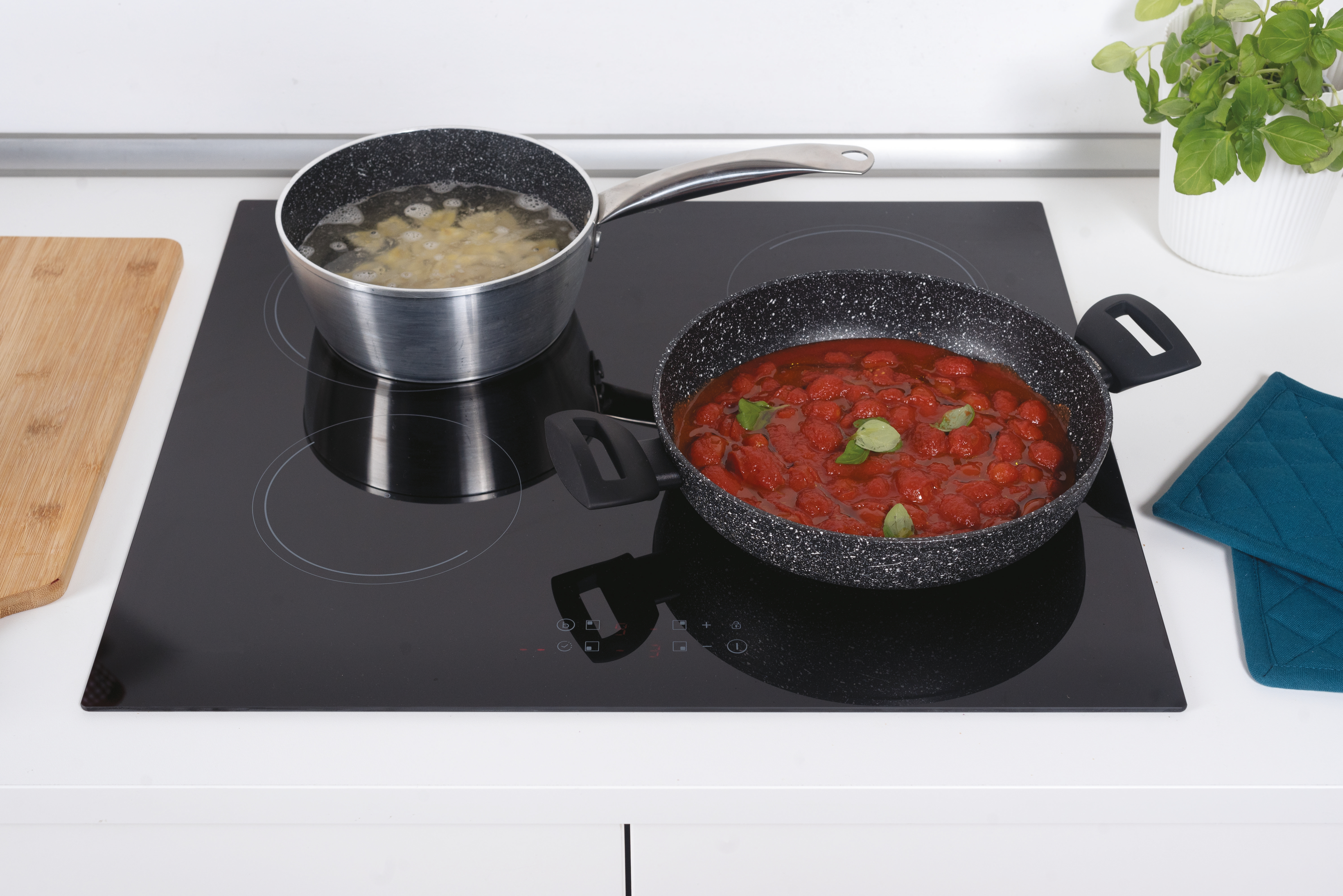 Un piano cottura nero con due pentole. Una con pasta, l'altra con salsa di pomodoro. Una pianta e presine.