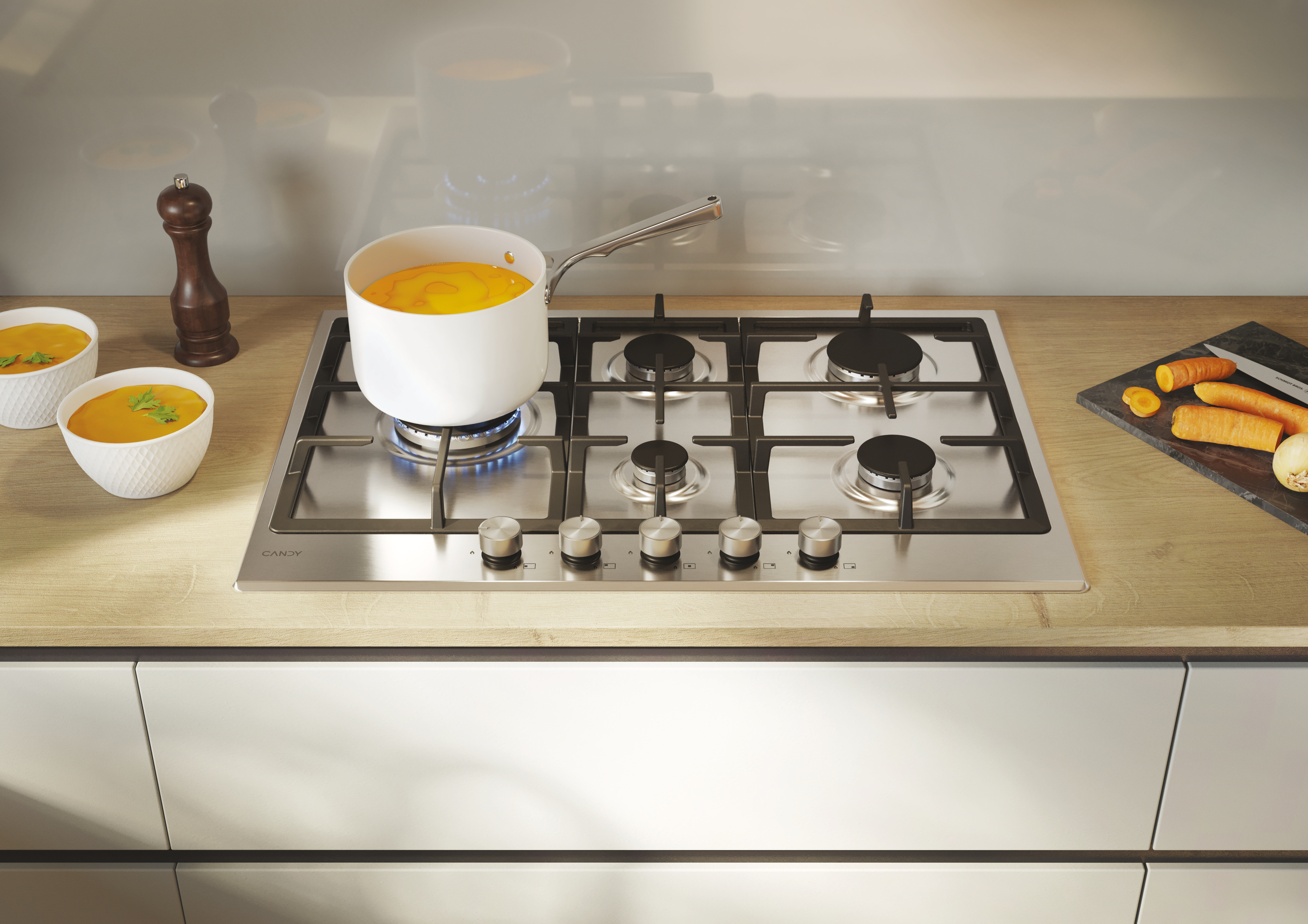Płyta gazowa ze stali nierdzewnej z garnkami, marchewkami i miskami z zupą na drewnianym blacie.