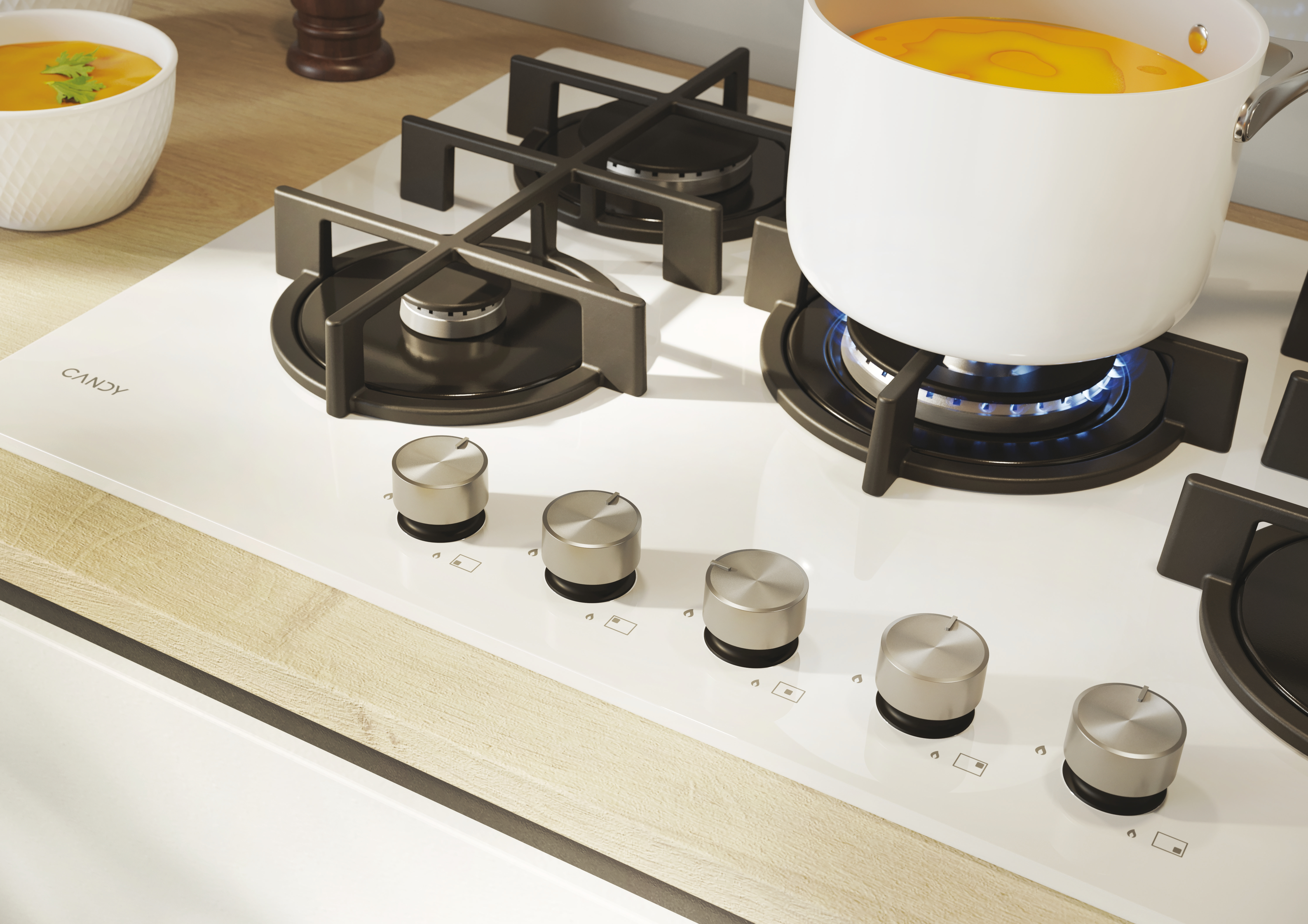 Biała płyta grzewcza z białym garnkiem na zapalonym palniku, miska z zupą i drewniany blat.