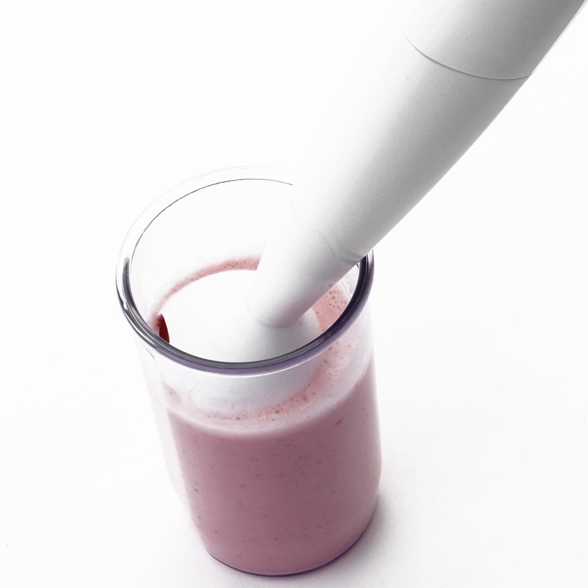 Una batidora de mano en un vaso con líquido rosa, mezclándolo sobre un fondo blanco.