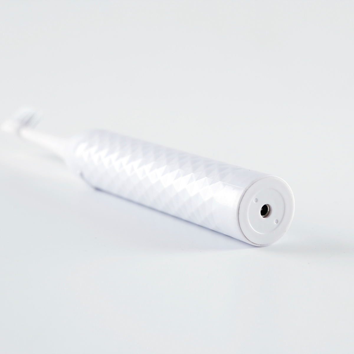 Cepillo de dientes eléctrico blanco sobre blanco. Tiene un mango texturizado. El cabezal del cepillo está a la izquierda.